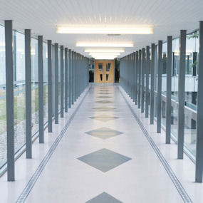 A brightly lit glass corridor leading to a door 