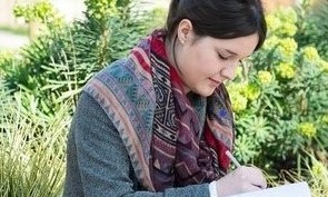 Image of female student sat outdoors studying a book