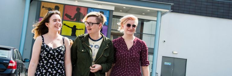 Three students walking together arm in arm outside the Martin Harris Centre