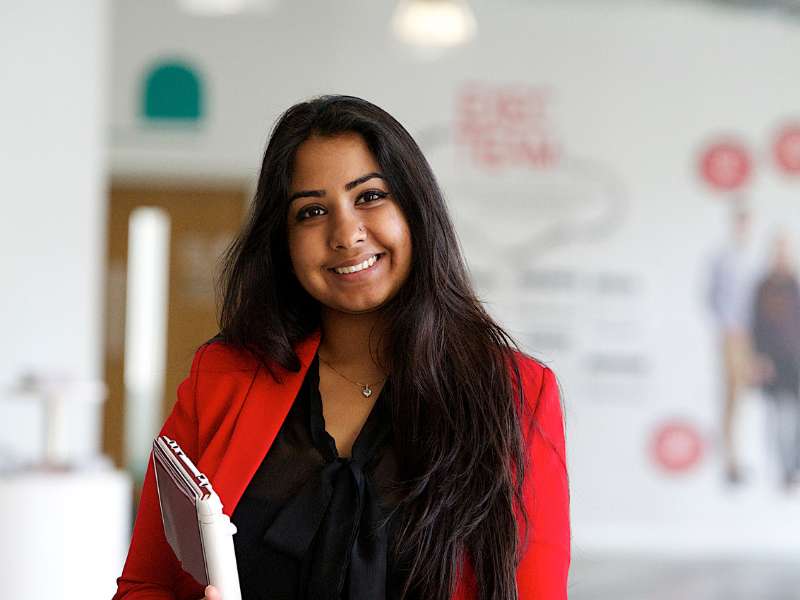 A young woman smiles at camera, holding a document