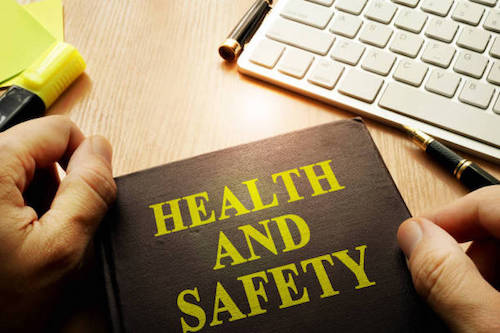 A Health & Safety book on a table with a mans hand about to open it