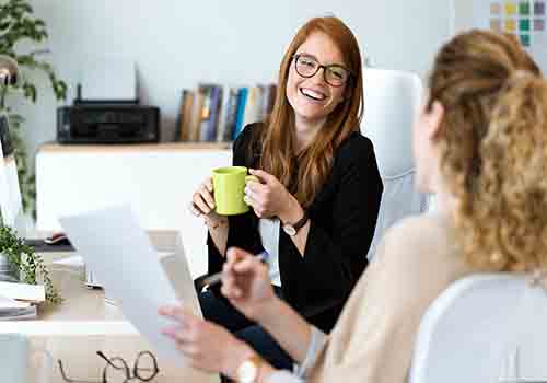 Two female colleagues talking over a coffee in work