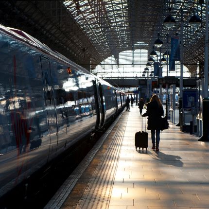 Woman in shadow with suitcase walking alongside a train platform