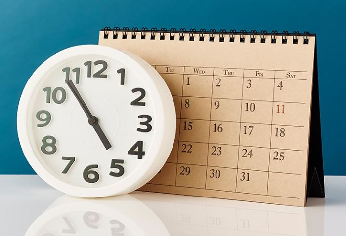 Picture of brown desk calendar behind a white clock at 4:55